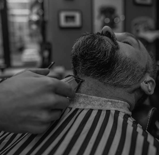 A man receives a beard trim from a barber in a well-lit barbershop setting.