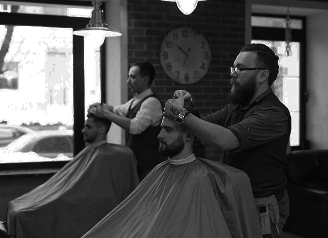 Barbers cutting hair of two customers seated in a modern barbershop with large windows and a wall clock in the background.